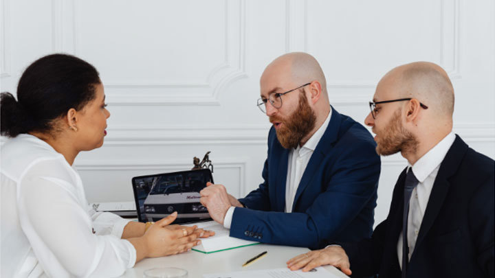 Three people in a meeting with a tablet and notebook having a discussion.